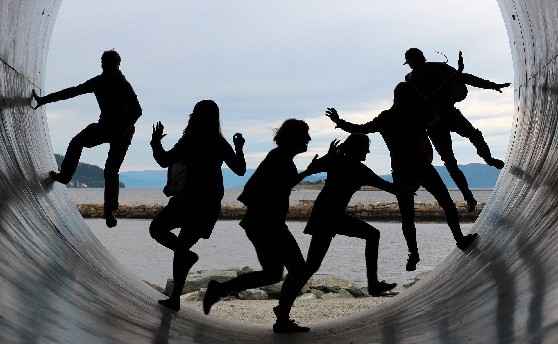 Meet the Team. Silhouettes of adults running on a large concrete tube or half pipe with water in background
