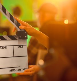 Film Studies A level. Hands holding empty clapperboard with film equipment and people blurred in background
