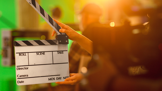 Film Studies A level. Hands holding empty clapperboard with film equipment and people blurred in background
