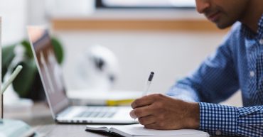 Man sat at desk with laptop & notepad