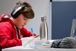 LearnOnline news article - what is an IGCSE? 12-14 year old boy in red jumper sat at desk studying with headphones