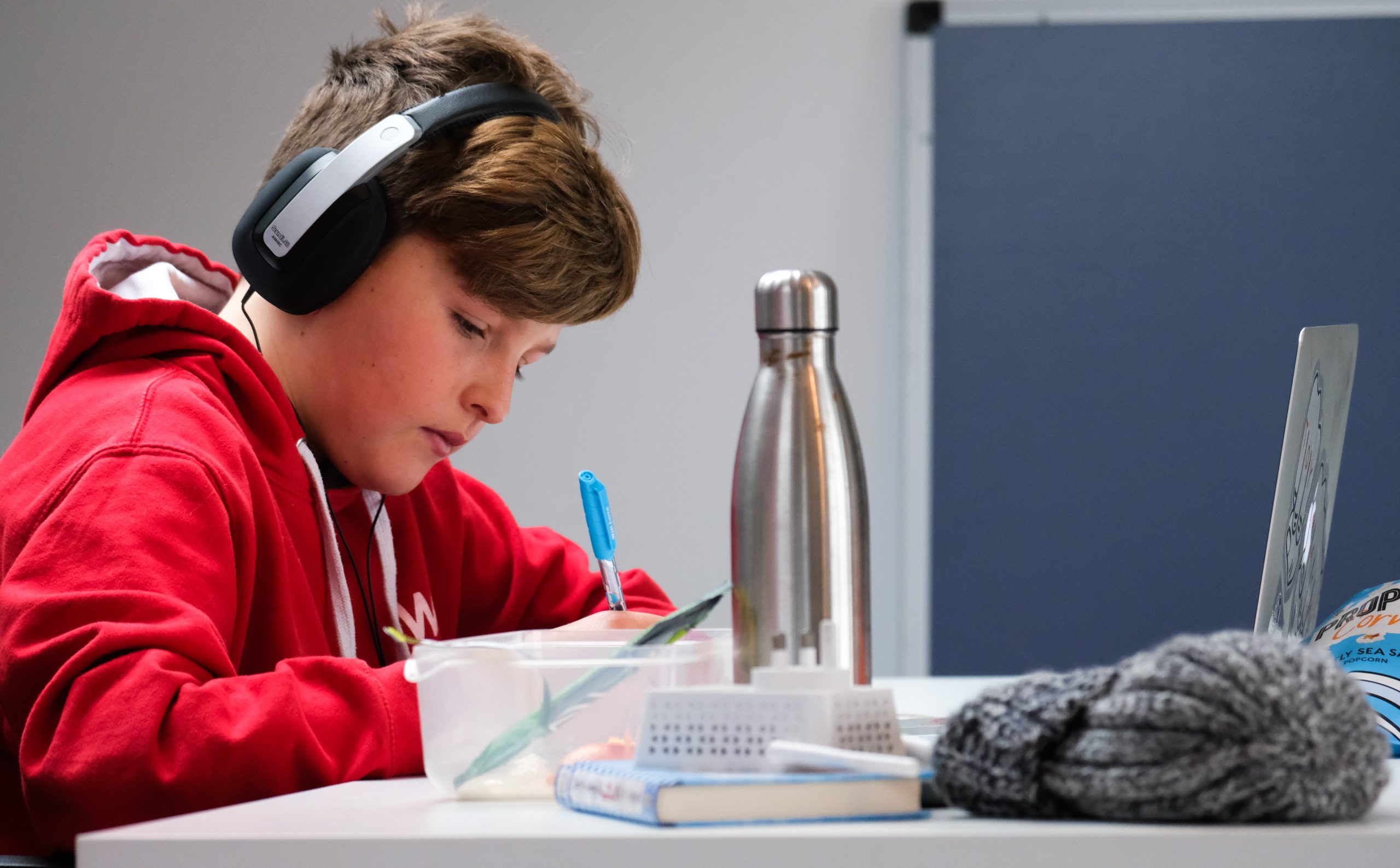 LearnOnline news article - what is an IGCSE? 12-14 year old boy in red jumper sat at desk studying with headphones