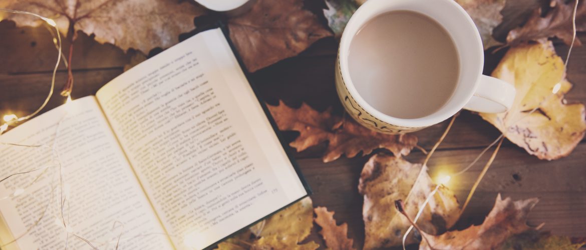 Enrol with us at any time news article Book, cup of tea and candle on a table with Autumnal leaves