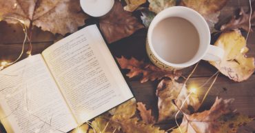 Enrol with us at any time news article Book, cup of tea and candle on a table with Autumnal leaves