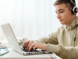 LearnOnline Live A levels package 16-18 year old boy with headphones on typing on a laptop