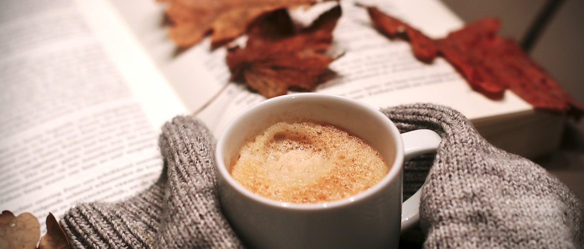 LearnOnline News September_Open book with Autumn leaves with jumper covered hands holding hot drink
