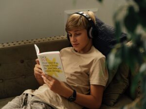 LearnOnline English IGCSE Package. Young teen sat on sofa reading a book with headphones on.