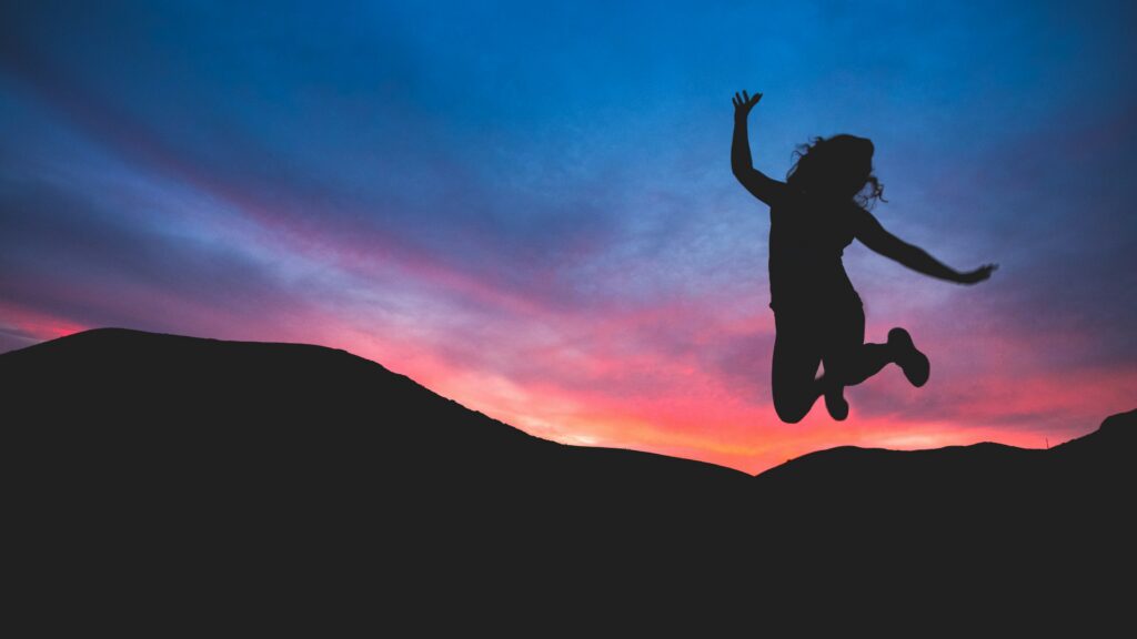 Silhouette of someone jumping in front of sunset behind mountains