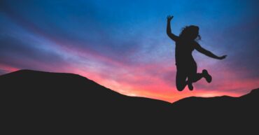 Silhouette of someone jumping in front of sunset behind mountains