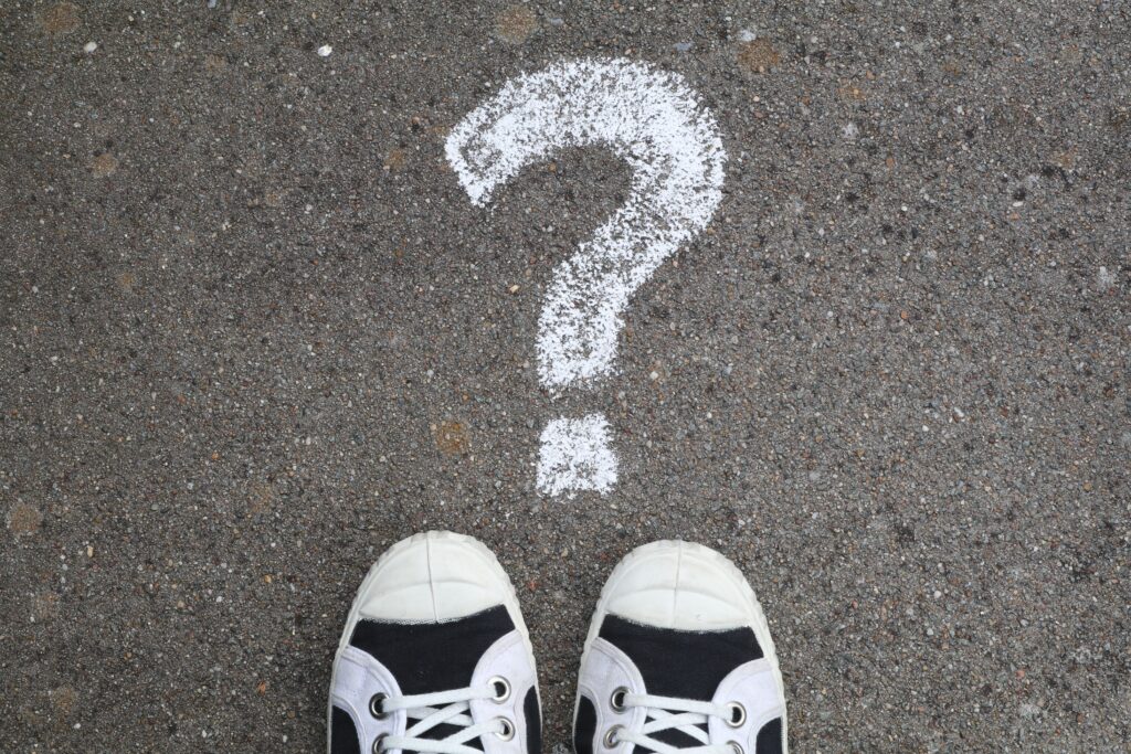 Tips of trainers pointing to question mark on pavement
