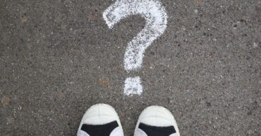 Tips of trainers pointing to question mark on pavement